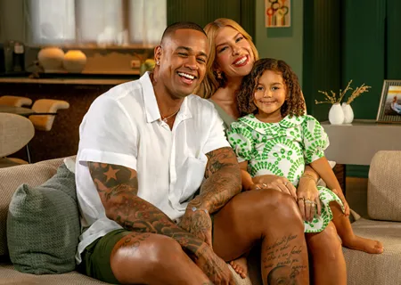  Leo Santana, Lore Improta e filha sorriem em sofá em casa 